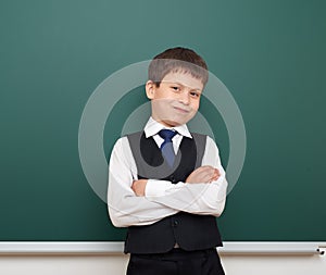 School student boy posing at the clean blackboard, grimacing and emotions, dressed in a black suit, education concept, studio