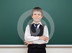 School student boy posing at the clean blackboard, grimacing and emotions, dressed in a black suit, education concept, studio