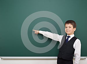 School student boy posing at the clean blackboard, show finger and point at, grimacing and emotions, dressed in a black suit, educ