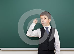 School student boy posing at the clean blackboard, show finger up and point, grimacing and emotions, dressed in a black suit, educ