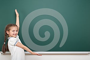 School student girl posing at the clean blackboard, grimacing and emotions, dressed in a black suit, education concept, studio pho