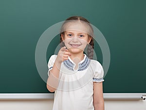 School student girl posing at the clean blackboard, grimacing and emotions, dressed in a black suit, education concept, studio pho