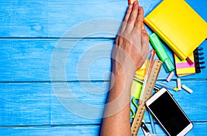 school students hand cleans away the school supplies on blue wooden table background. student prefers to perform other tasks.