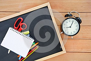School supplies on ablackboard lying on a table next to an alarma clock