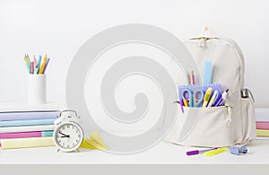 School supplies and backpack on table over white wall background