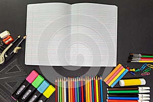 School supplies on black board background, with open notebook. Education, back to school concept with copy space
