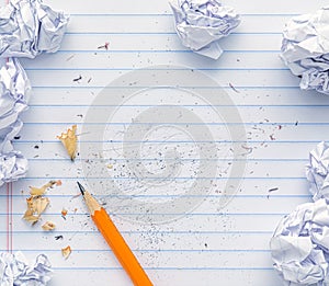 School supplies of blank lined notebook paper with eraser marks and erased pencil writing, surrounded by balled up paper