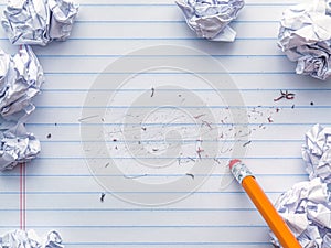 School supplies of blank lined notebook paper with eraser marks and erased pencil writing, surrounded by balled up paper and a photo