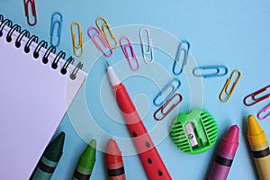 School supplies on a blue background. Back to school concept. Top view, copy space. Open paper notebook, pen, sharpener, crayons