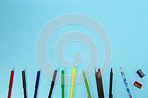 school supplies at the bottom of a pastel blue background, felt-tip pens, pen, copy space above