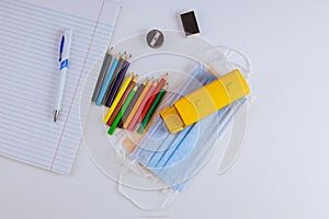 School supplies colored pencils on a safe coronavirus COVID-19 pandemic medical hygienic masks