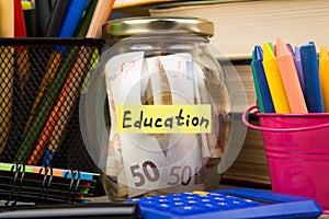 School supplies and glass jar with money for education on wooden table
