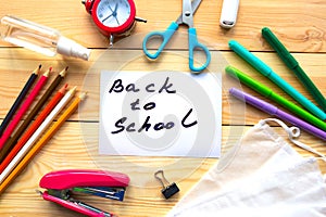 School supplies, medical mask and card with message Back to School on wooden background.