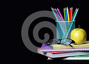 School Supplies over black. An apple, colored pencils