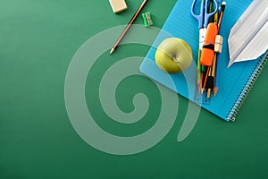 School supplies paper plane and apple on green background top