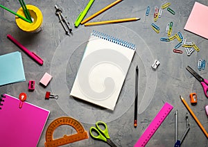 School supplies for school: notepad, pencils, pink ruler, compasses scattered on a gray table. Top view.