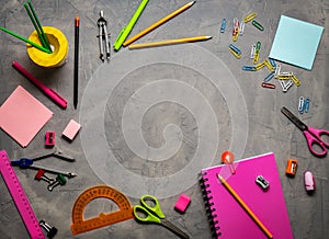 School supplies for school: notepad, pencils, pink ruler, compasses scattered on a gray table. Top view.