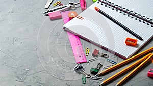School supplies for school: notepad, pencils, pink ruler, compasses scattered on a gray table. Top view.