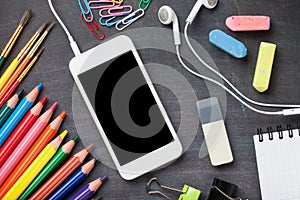 School supplies and smartphone on blackboard background