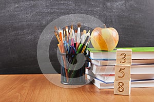 School supplies with a stack of books and an apple on blackboard background with copyspace for your text, design. Back