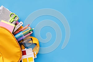 School supplies sticking out of a backpack on a blue background. Back to school concept