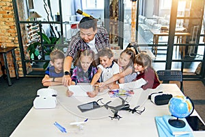 School teacher at desk works with five young pupils using digital tablet computer in technology class. Development