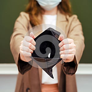 School teacher in a medical mask with a hole in the wallet with no money