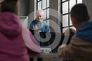 School teacher standing in front of pupils and writing notes in computer classroom at school