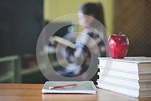 School themed image comprising an apple and a pile of books The background is a student sitting reading a book