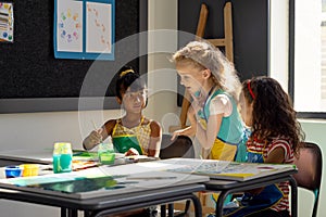 In school, three young girls are focusing on painting in art class
