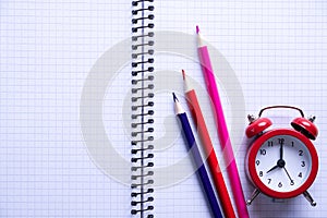 School time minimalist concept. Colored pencils and notebooks and a red alarm clock.