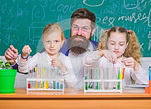 School time. Schoolgirls holding test tubes guided by teacher. School children performing experiment in science
