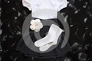 School uniform with white shirt, socks and dark denim skirt on a black background. Flatlay, top view, copy space