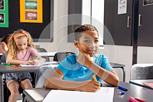 In school, young biracial male student sitting at a desk in a classroom, looking thoughtful photo