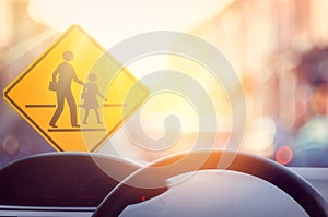 School zone warning sign and inside car view ,steering wheel on blur traffic road with colorful bokeh light abstract background