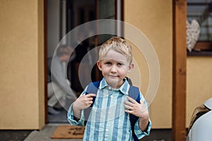 Schoolboy with backpack on back standing in frotn of house. Preparation for school day, morning.