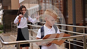 A schoolboy boy standing near the school, a girl covers his eyes with her hands.