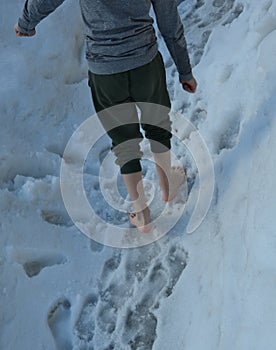 Schoolboy boy walks barefoot through the snow covering the school yard. He is dressed in sweatpants and a thermal shirt. walking t