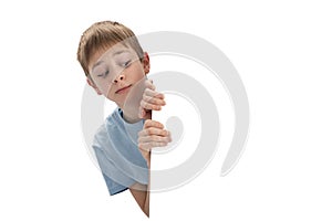 Schoolboy cautiously peeks out from behind board with empty space. Boy looks out from behind banner. Copy space