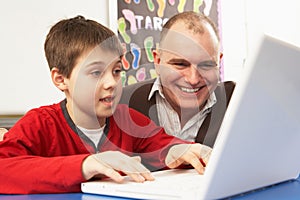 Schoolboy In IT Class Using Computer With Teacher