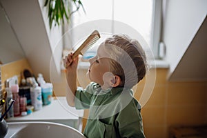 Schoolboy combing hair in the morning before going to school. Morning routine for schoolkids.