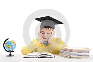 Schoolboy does homework sitting at desk in isolation on white background. Boy in students hat reading textbook