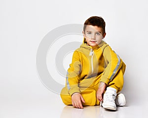 Schoolboy dressed in a stylish yellow sports suit and white sneakers poses on a white background.