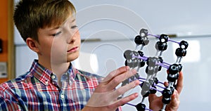 Schoolboy experimenting molecule model in laboratory at school