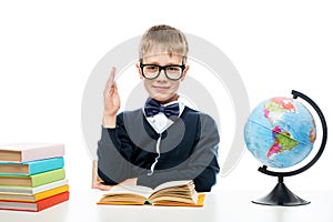 A schoolboy with glasses at a table with books and a globe pulls