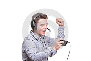 Schoolboy guy with headphones playing on mobile phone. Teenager happy screams . Young man won an online game on a smartphone.
