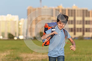 The schoolboy happily runs with a backpack on the field against the background of the city landscape