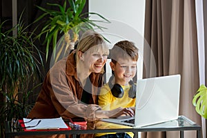 Schoolboy in headphones with mother do a school lessons via computer at home