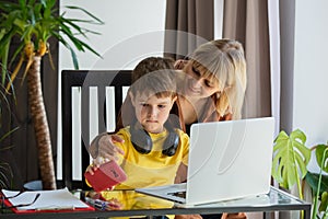 Schoolboy in headphones with mother do a school lessons via computer at home