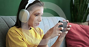 Schoolboy in Headphones Playing on Phone and Expressing Amazement on Couch
